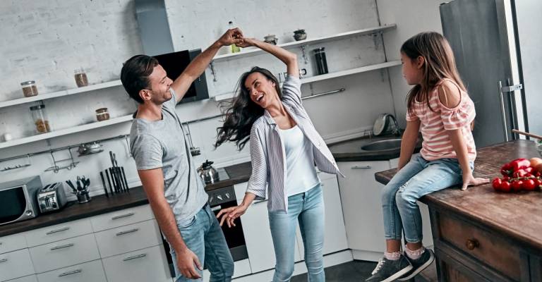 Dansend stel in keuken terwijl kind toekijkt zittend op aanrecht